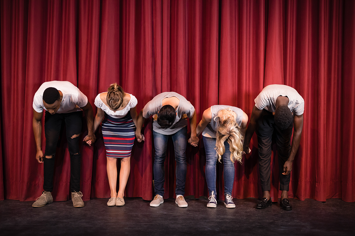 Performers bow in front of a red stage curtain